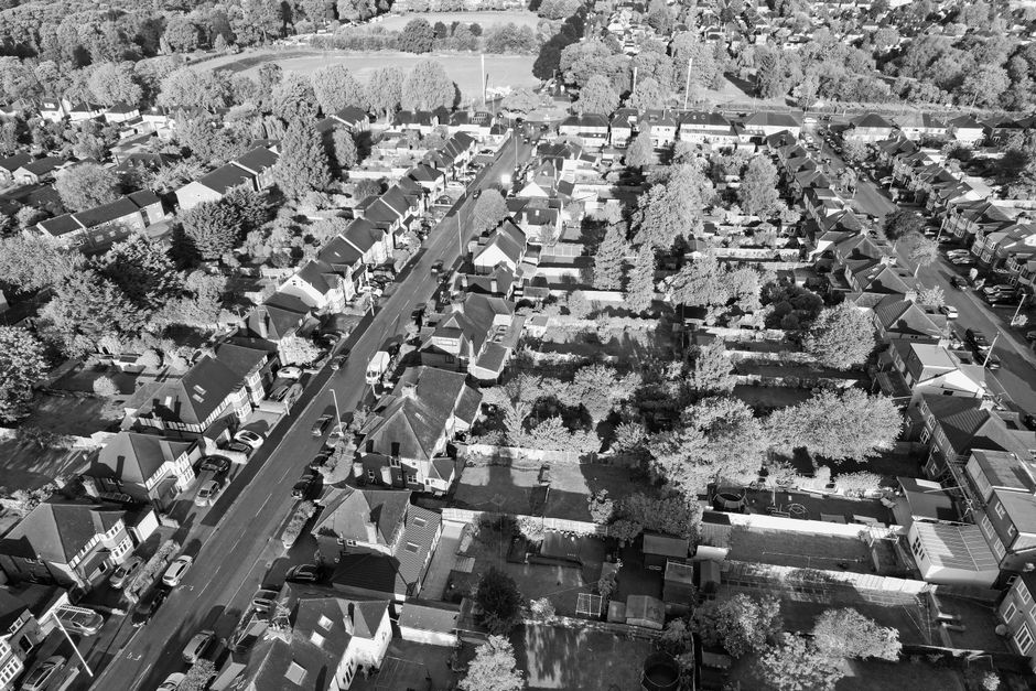 A black and white aerial photograph of a residential neighborhood with a street running vertically through the center. The image shows numerous detached and semi-detached houses with pitched roofs, so